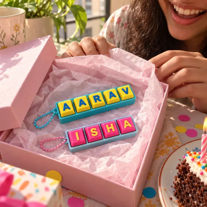 Two Fidget Clicker keychains in an opened pink gift box on a table set for a birthday.